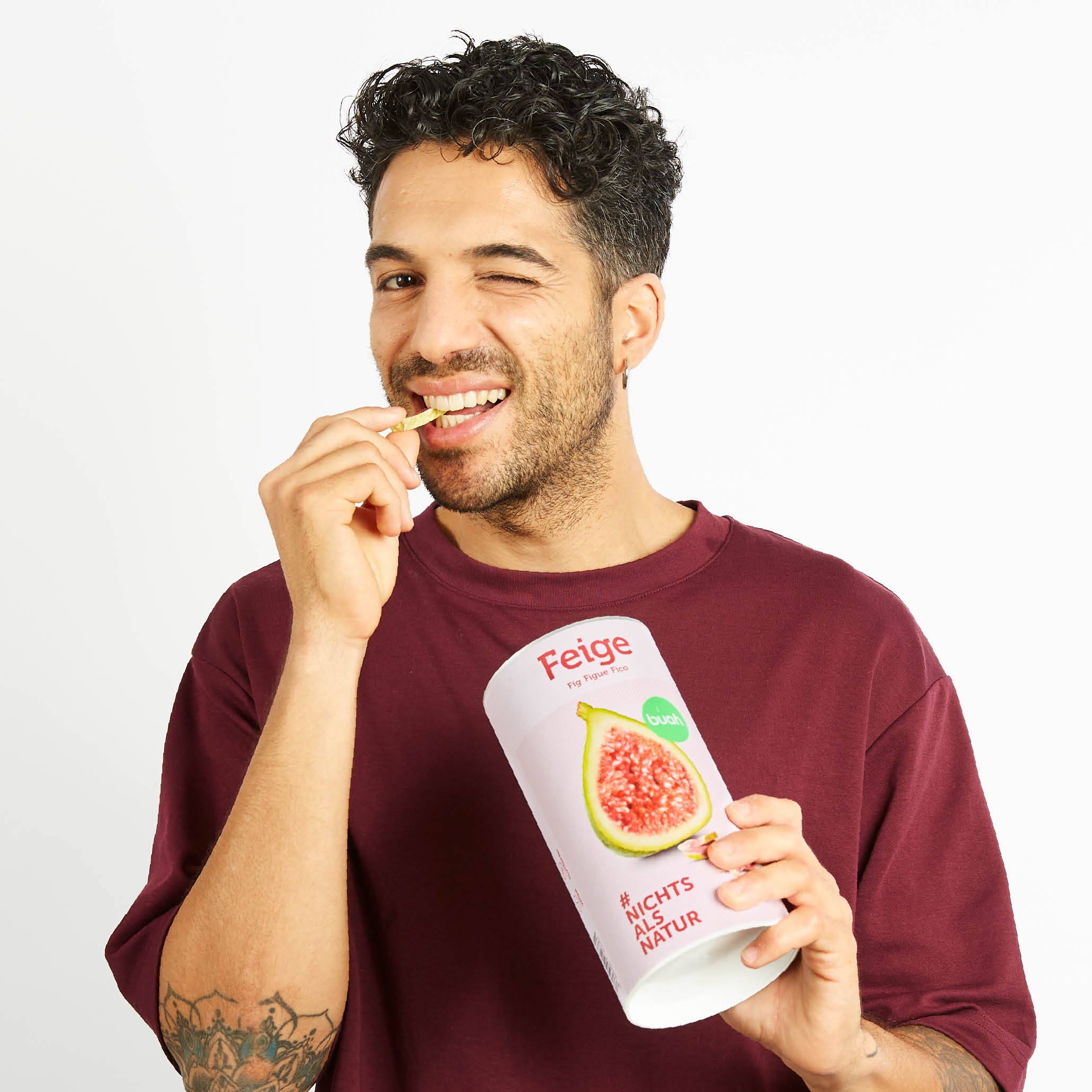 Junger Mann zwinkert in die Kamera und isst gefriergetrocknete Feige von buah aus der Dose