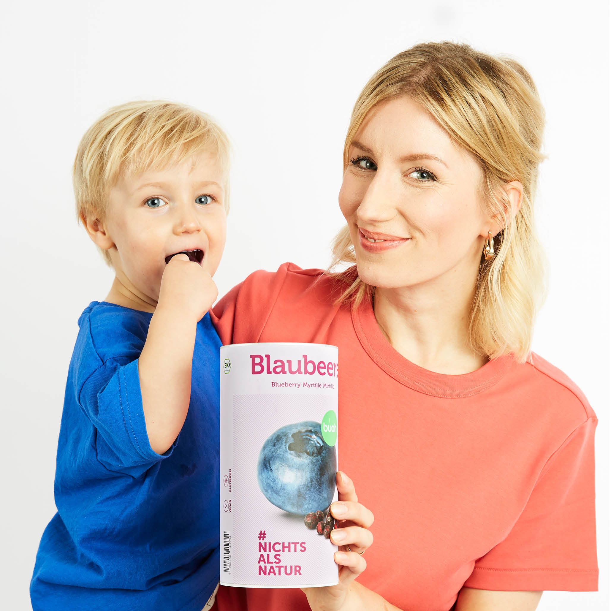Mama mit Sohn auf dem Arm hat eine Dose buah Blaubeeren in der Hand und Kleinkind isst Blaubeeren