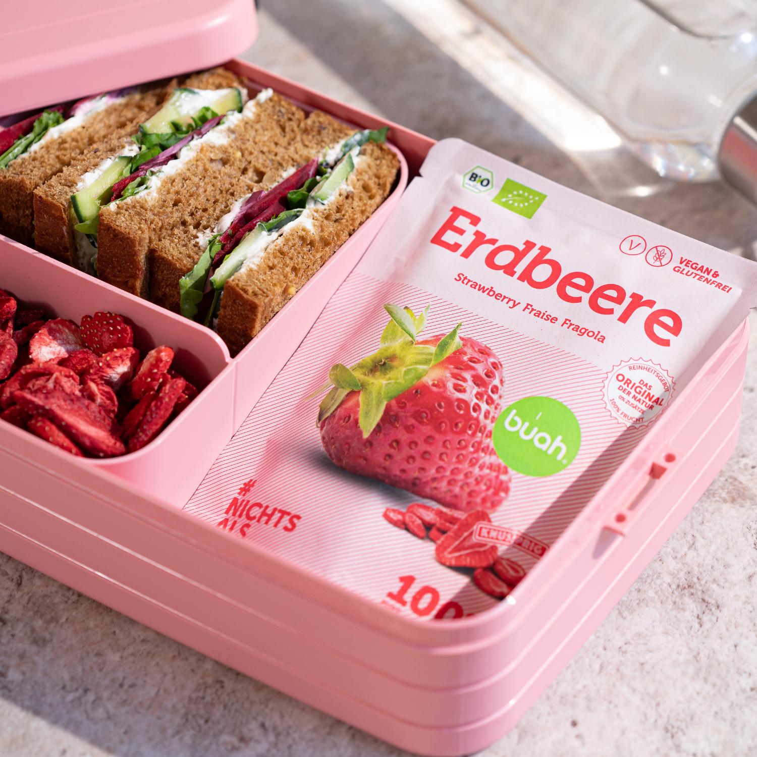 Snackpack buah Erdbeeren in einer rosa Brotdose neben gefriergetrockneten Erdbeeren und einem Sandwich