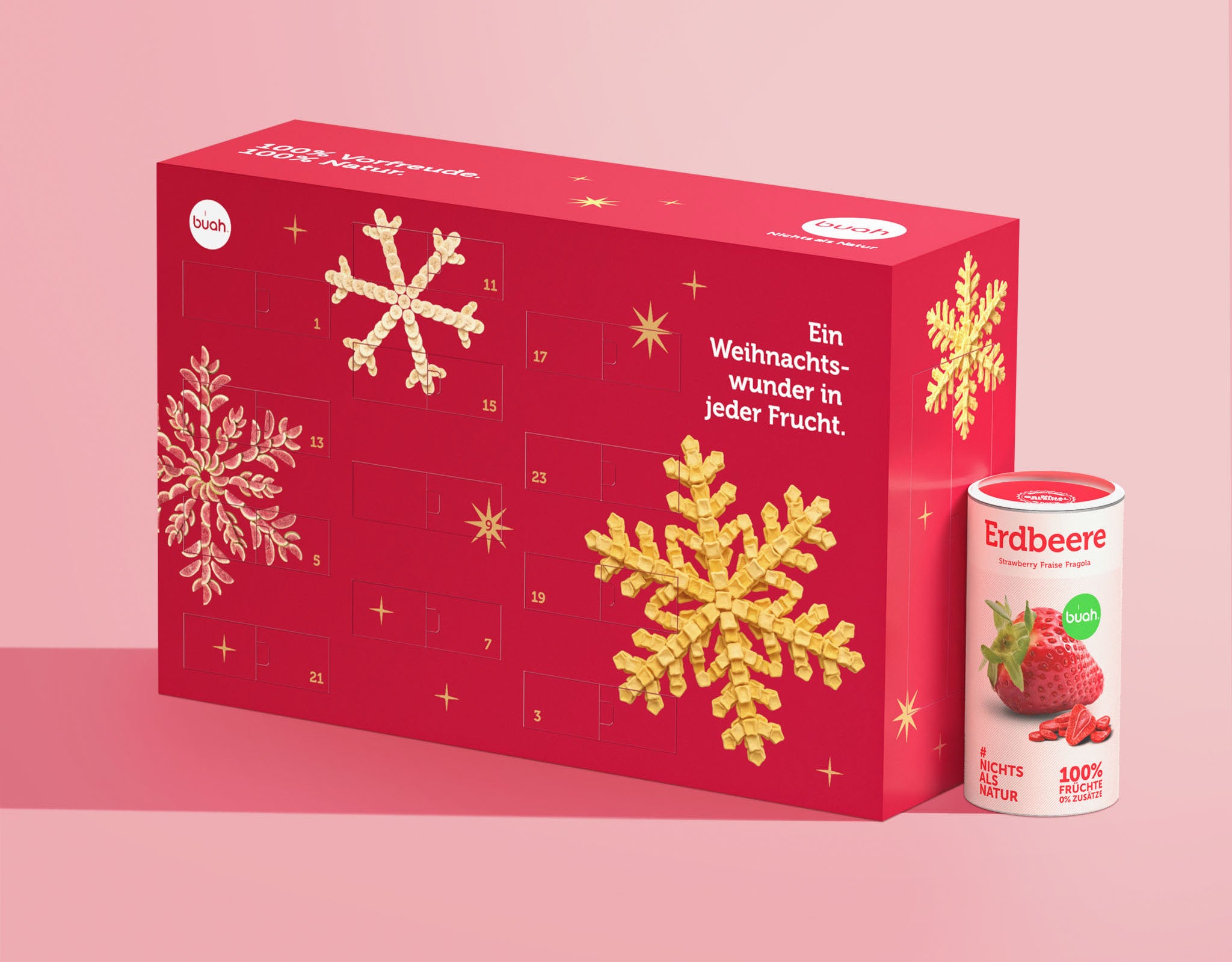 Der rote buah Adventskalender steht neben einer großen Dose buah gefriergetrocknete Erdbeeren vor einem zartrosa Hintergrund. Auf dem Kalender sind Schneeflocken aus Fruchtstücken abgebildet.