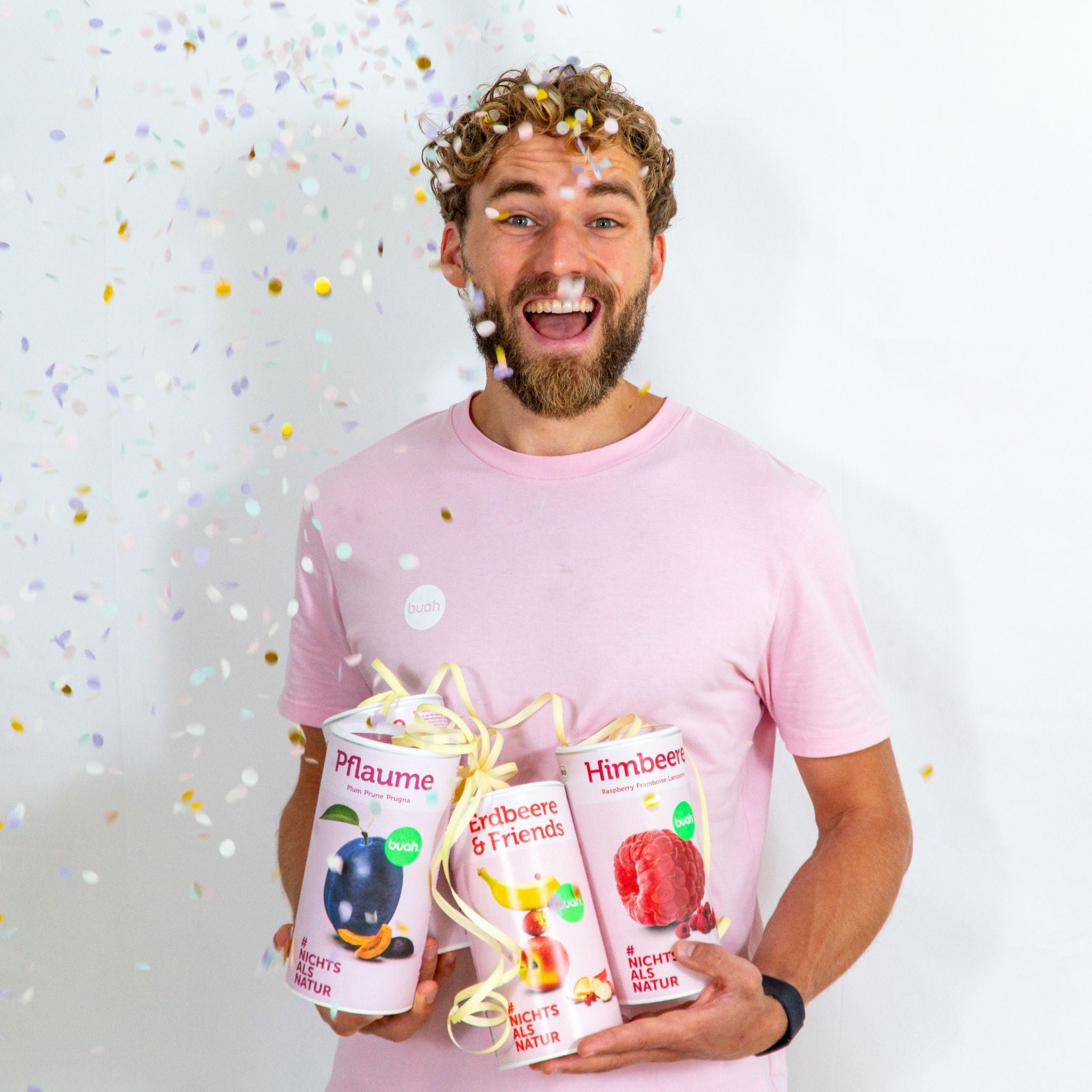 Daniel Gruender von buah in rosa buah Shirt mit buah gefriergetrockneten Fruechten in der Dose im Arm - Konfetti und Luftschlangen im Hintergrund fuer den buah Birthday