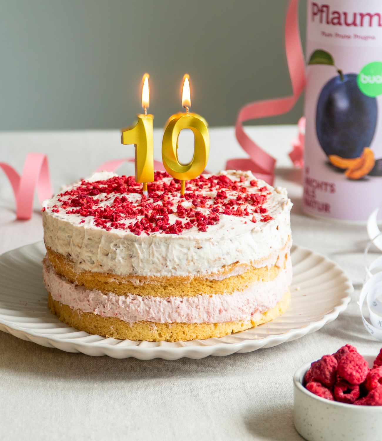 buah Geburtstagstorte mit zwei Schichten aus buah gefriergetrockneter Pflaume und Himbeere auf einem Teller mit goldenen Kerzen, die eine 10 darstellen und brennen