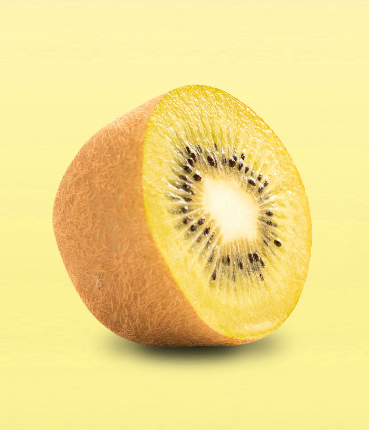 Eine angeschnittene Hälfte einer frischen Goldenen Kiwi liegt schräg vor einem hellgelben Hintergrund und zeigt ihr saftig gelbes Fruchtfleisch.