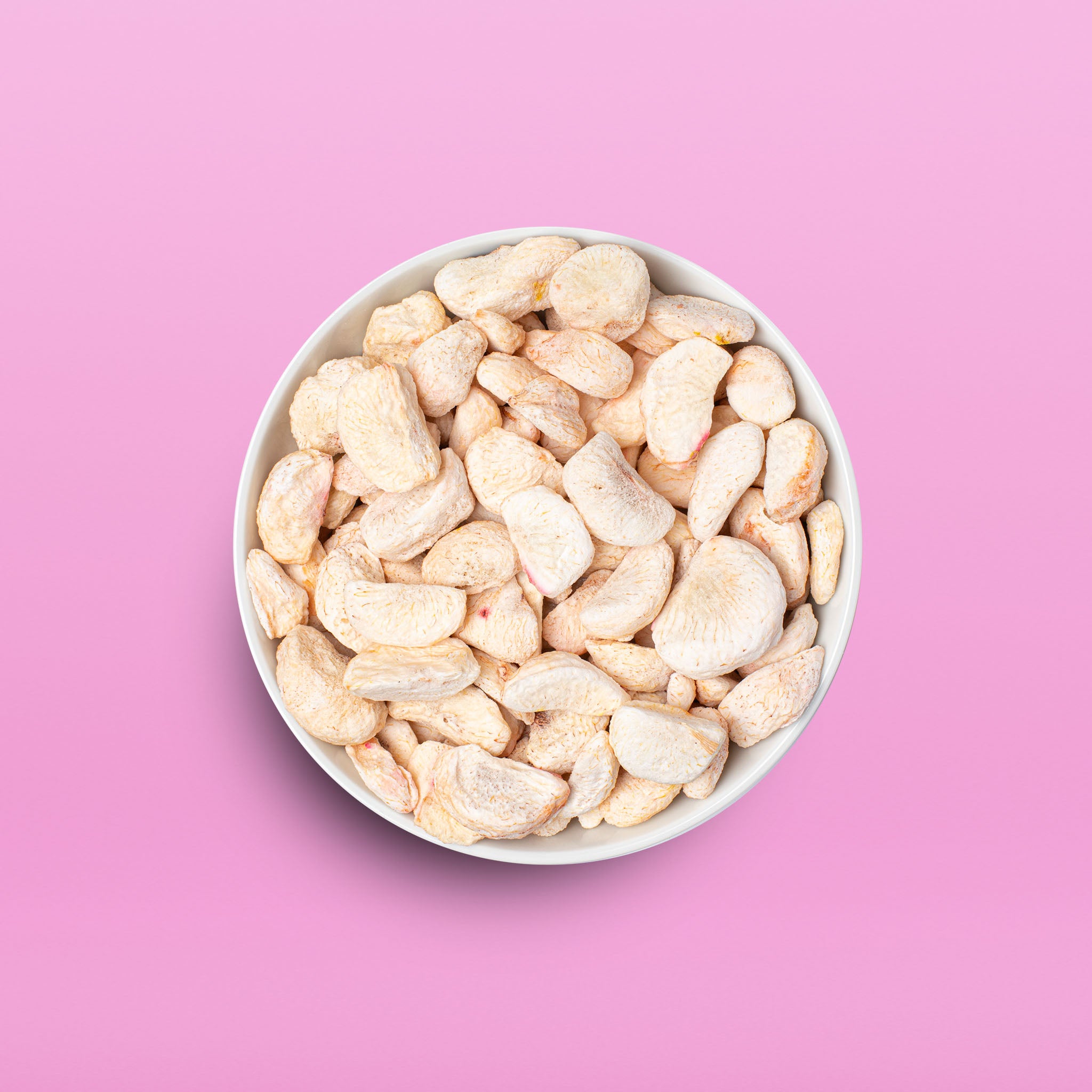 Die Draufsicht auf eine weiße Schüssel, die prall gefüllt ist mit hellen, buah gefriergetrockneten Mangostan-Stücken, platziert auf einem pinken Hintergrund.