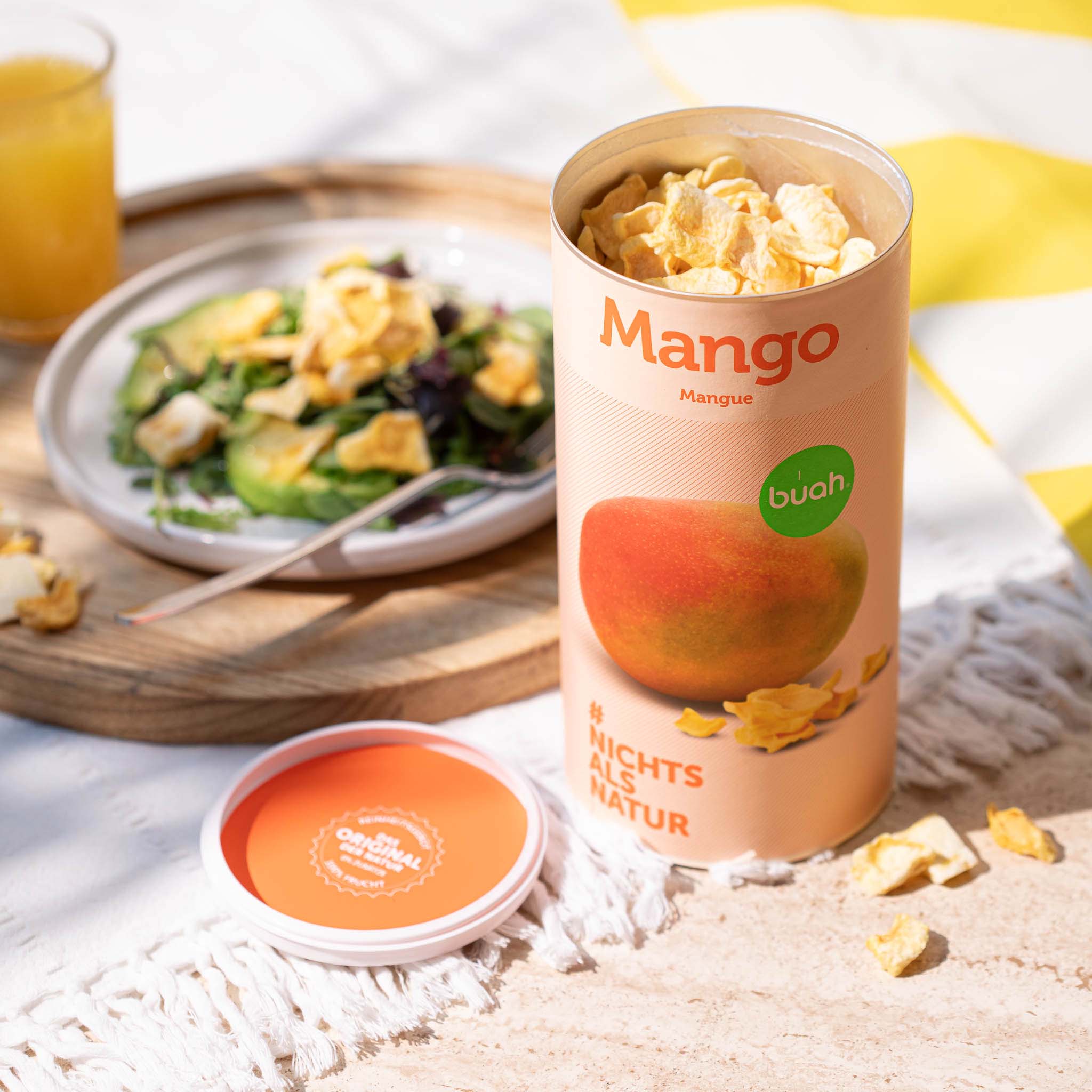 Dose buah Mango steht neben einem Teller mit Salat und gefriergetrockneter Mango als Topping