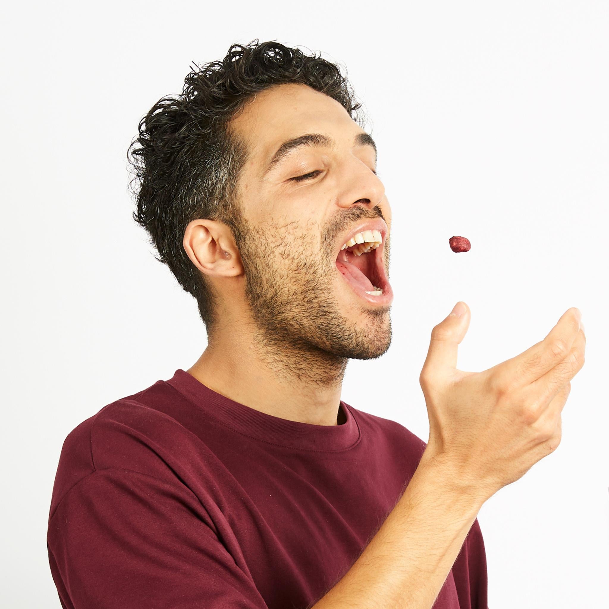 Junger Mann in dunkelrotem Shirt wirft sich eine buah gefriergetrocknete Sauerkirsche in den Mund