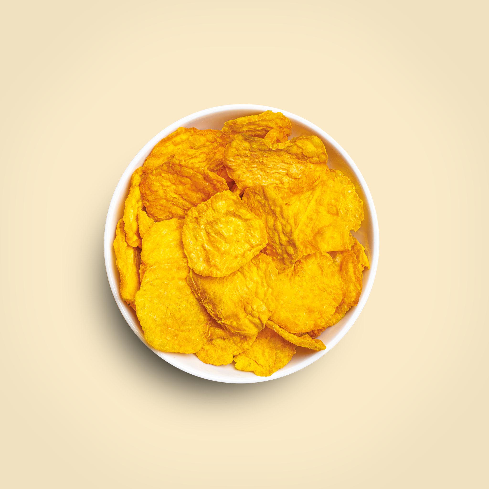 buah Gelbe Bete Chips in einer weißen Schale vor gelbem Hintergrund