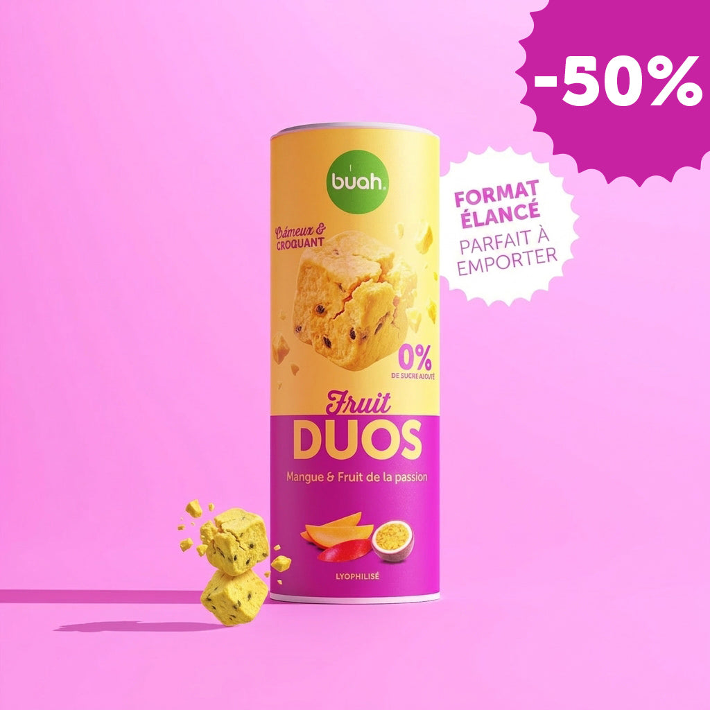 Une boîte Slim de buah Fruit DUOS Mangue & Fruit de la passion se trouve au centre devant un fond rose. À côté se trouve une bulle blanche en forme d'étoile avec le texte « BOÎTE SLIM PARFAITE À EMPORTER ». Des cubes de fruits flottent à gauche.