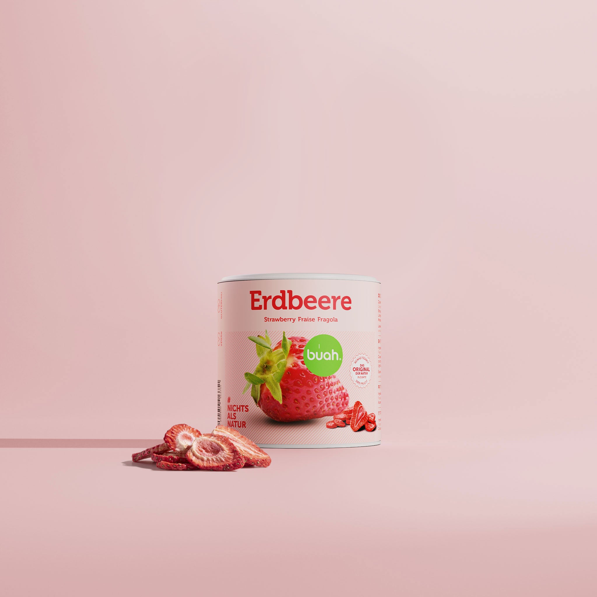 Eine breite Maxipack-Dose buah gefriergetrocknete Erdbeeren steht vor einem pinken Hintergrund. Davor liegen einige knusprige Erdbeerscheiben.