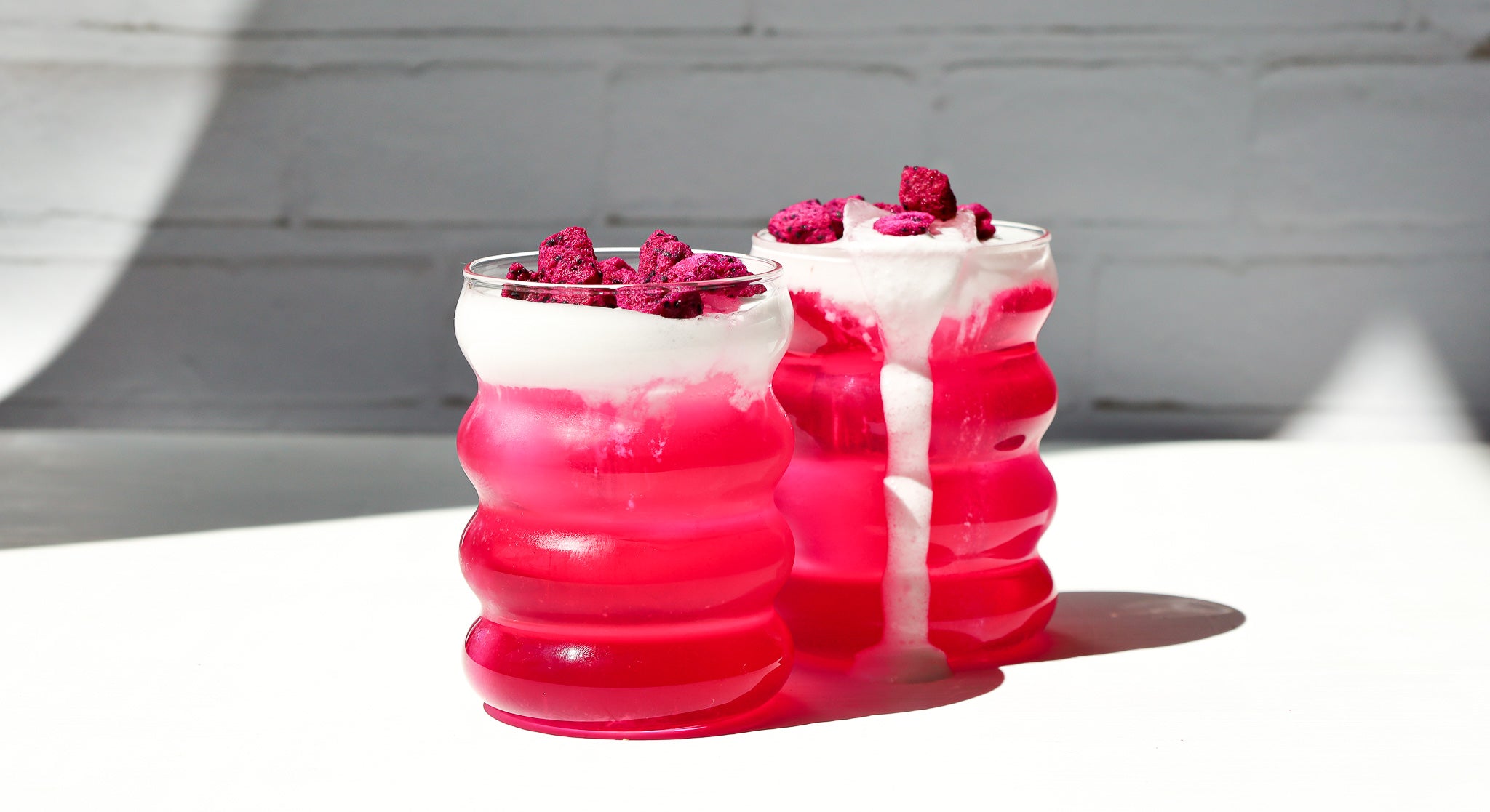 Zwei Bubble Gläser gefuellt mit pinker Limonade und Cold Foam on top, garniert mit buah gefriergetrockneter Drachenfrucht