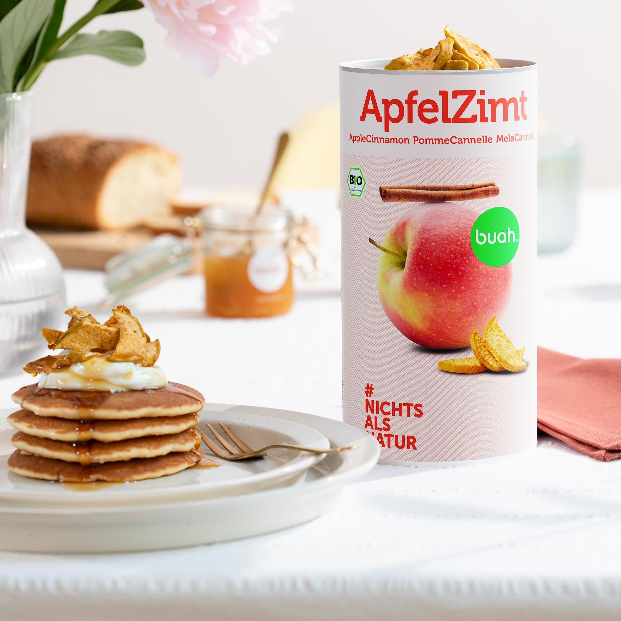 Weihnachtliche Pancakes gestapelt auf einem weissen Teller, getoppt mit Honig und knusprigem buah ApfelZimt, daneben eine buah Dose ApfelZimt