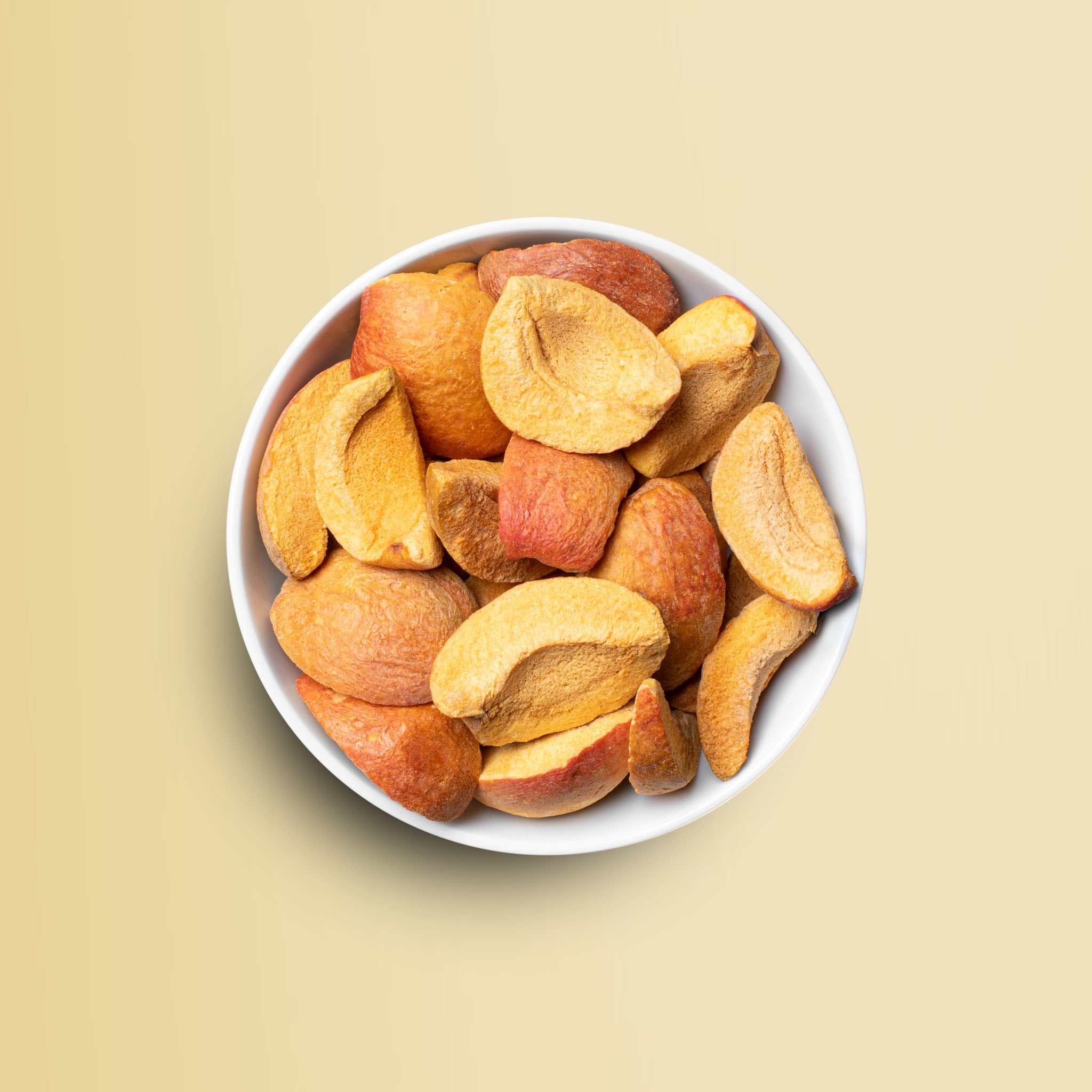 Weisse Schale vor gelbem Hintergrund gefuellt mit buah gefriergetrockneter Aprikose in Schnitzen, dunkel gelb, reif gefaerbt 