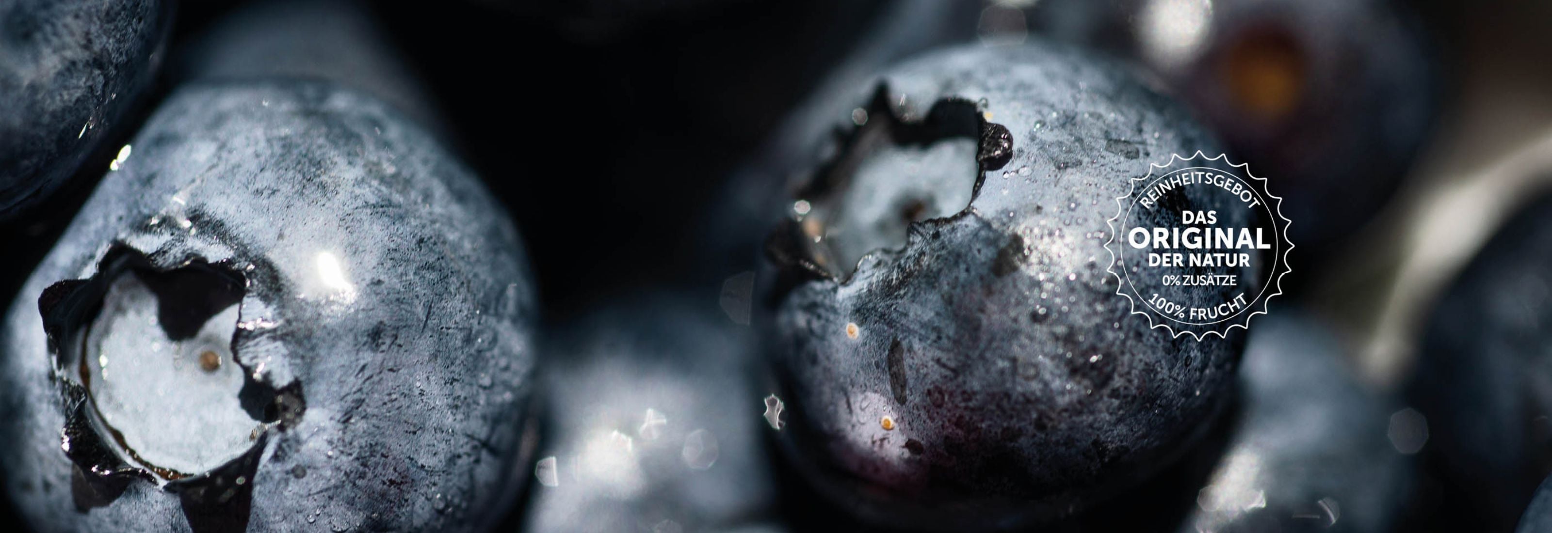 Frische, dunkelblaue, mit Wasser benetzte Blaubeeren in der Nahaufnahme mit einem Badge des buah Reinheitsgebot auf dem Bild