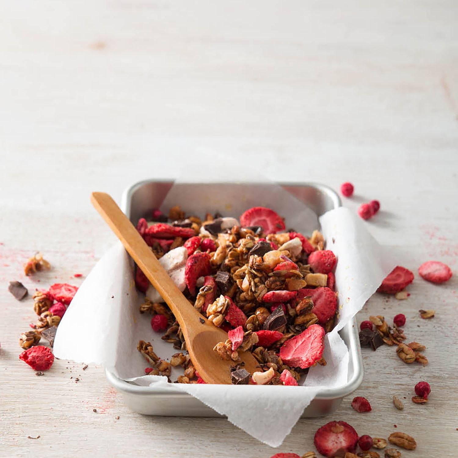 Selbstgemachtes Granola mit buah gefriergetrockneten Erdbeeren in einer flachen Schale aus Metall mit einem Holzlöffel im Granola
