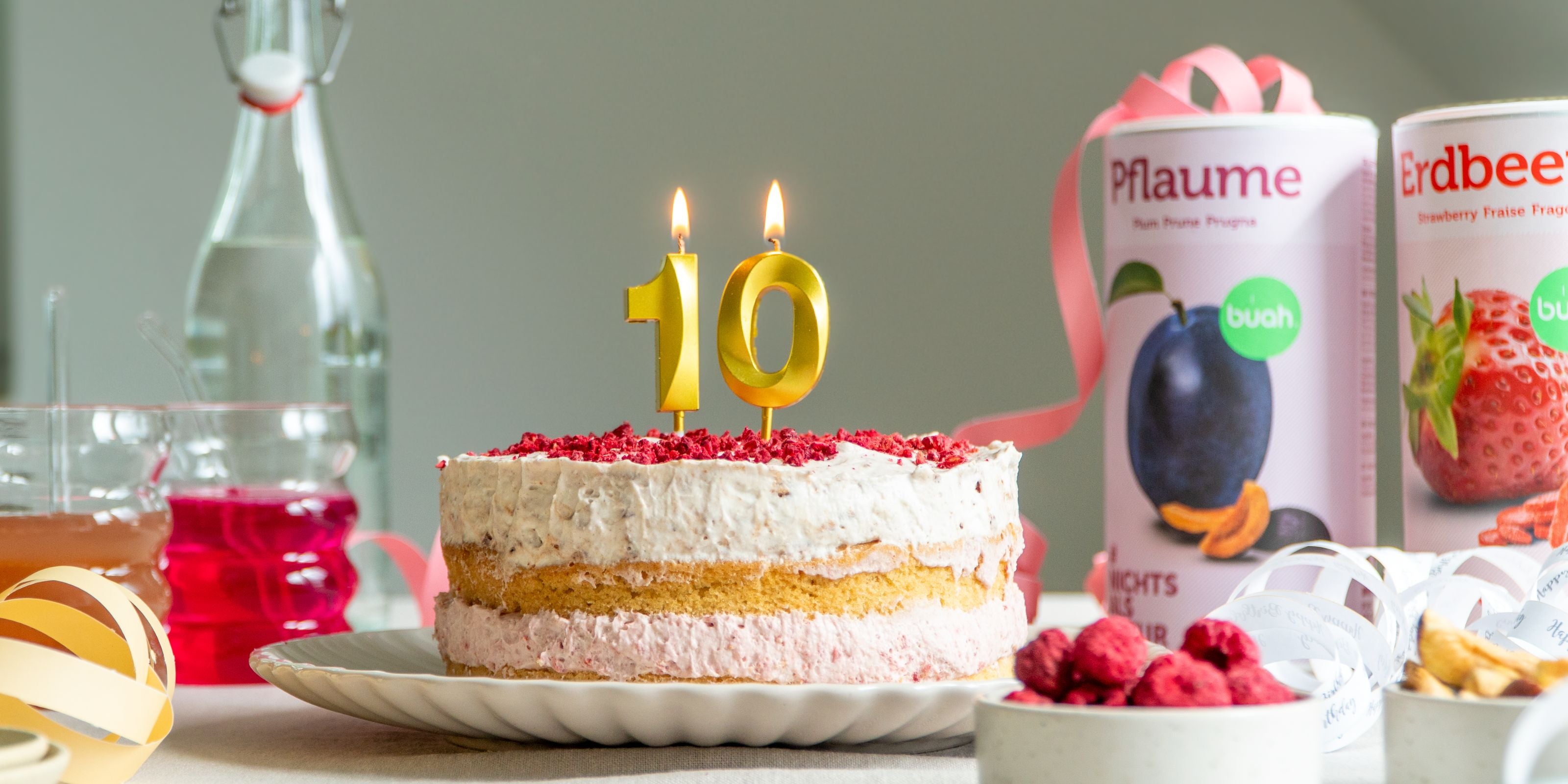 buah Geburtstagstorte mit zwei Schichten aus buah gefriergetrockneter Pflaume und Himbeere auf einem Teller mit goldenen Kerzen, die eine 10 darstellen und brennen