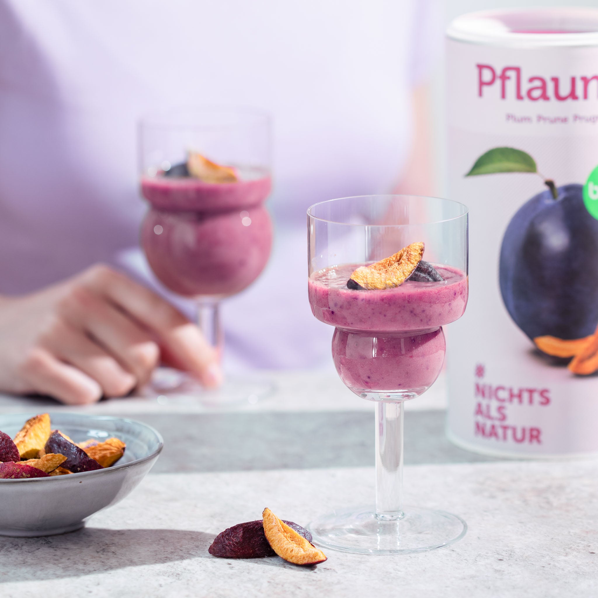 Dessertbecher mit einem Joghurt Dessert und Pflaume stehen auf einem Tisch, daneben eine Schale buah gefriergetrockneter Pflaumen und eine Dose buah Pflaume