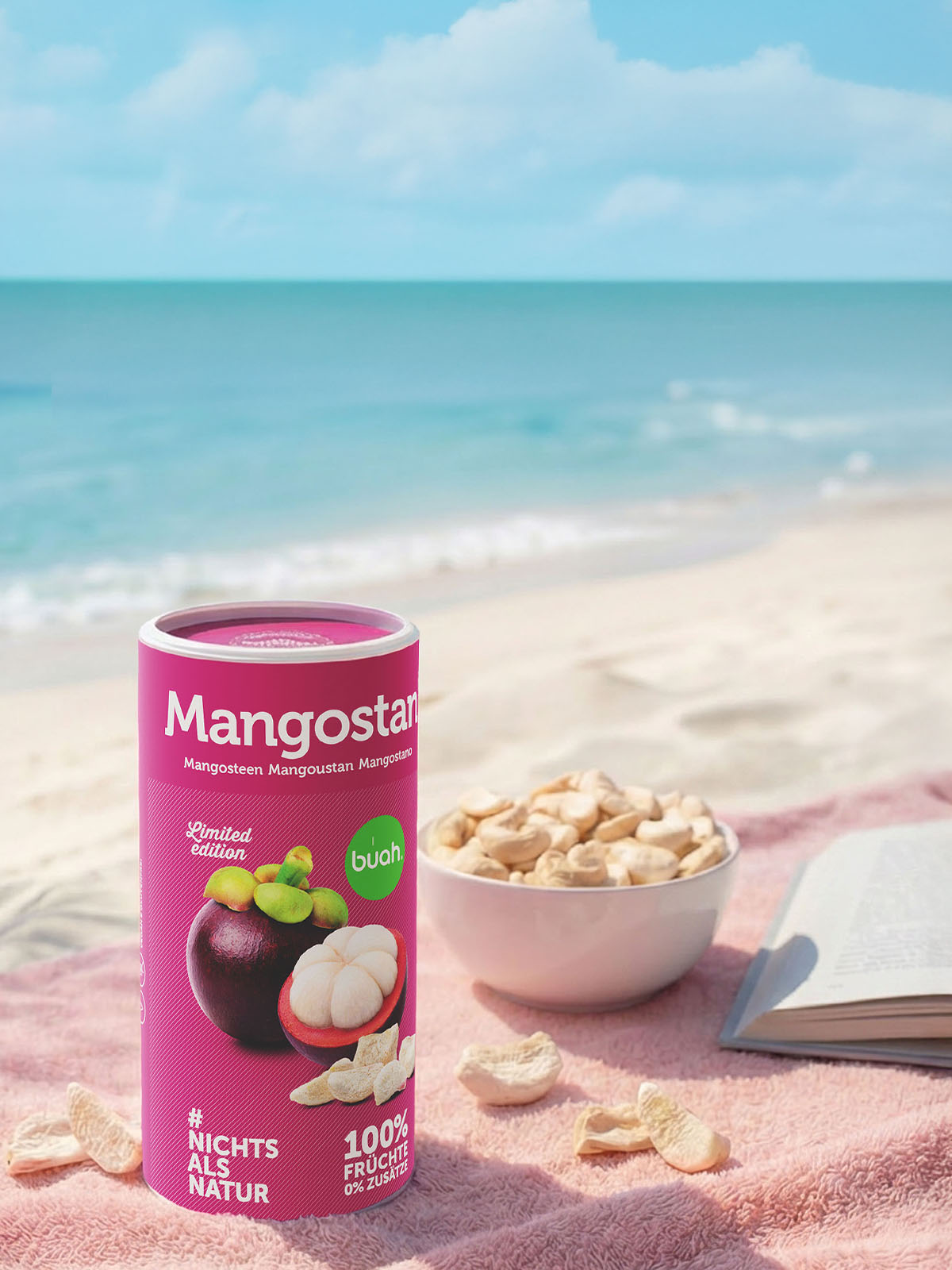 Ein Hochformat-Bild am Strand. Auf einem rosafarbenen Handtuch im Sand stehen eine Dose buah gefriergetrocknete Mangostan und eine Schale mit Fruchtstücken. Im Hintergrund rauscht das blaue Meer.