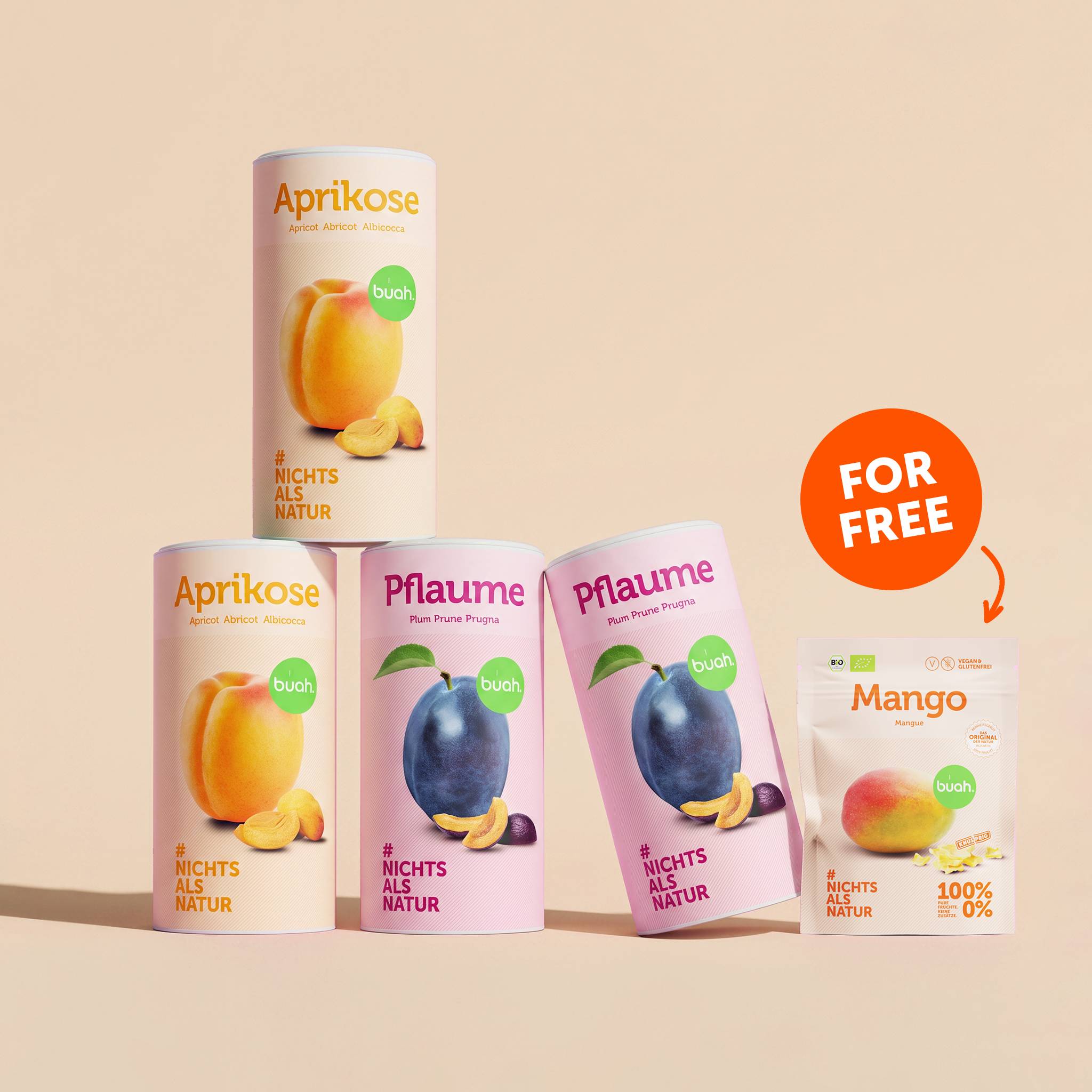 Eine Pyramide aus vier großen Dosen buah gefriergetrocknete Früchte (zwei Dosen Aprikose, zwei Dosen Pflaume) vor einem beigefarbenen Hintergrund. Rechts daneben steht ein kleiner Beutel Mango mit einem „FOR FREE“-Hinweis.